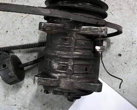 Compresor usado con la polea del embrague, el cable de la bobina y la correa suelta, sobre el suelo del taller.