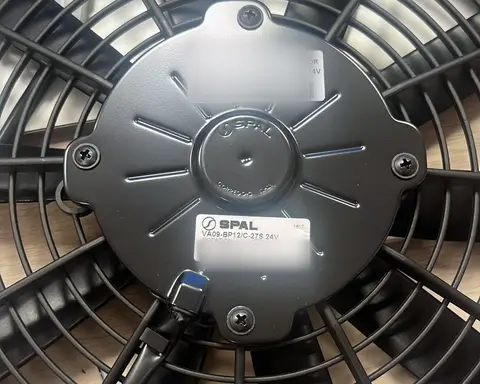 Electroventilador visto por el lado del motor, con la rejilla y el cable de conexión.