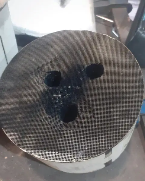 Cara de un monolito de escape con tres huecos abiertos en el panal, sobre el banco.
