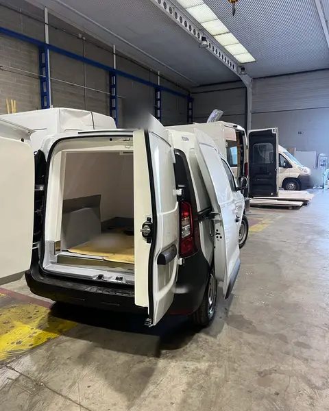 Furgoneta con las puertas traseras abiertas y la caja isoterma vacía, con cartón en el suelo, dentro de la nave.