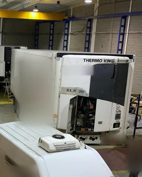 Dos semirremolques frigoríficos en la nave, uno con el equipo Thermo King abierto, y delante el techo de una furgoneta con una unidad montada encima.