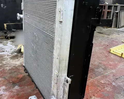 Radiador de aluminio de gran tamaño, con bastidor metálico y bocas de conexión, colgado de cadenas en la nave.