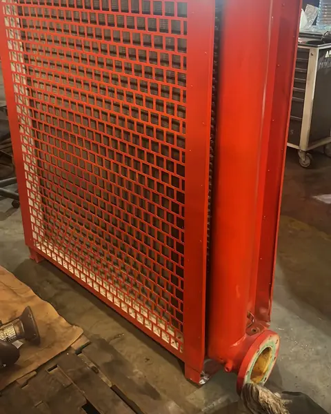 Intercambiador de calor industrial pintado en rojo, visto por la cara protegida con una rejilla metálica, con la brida de conexión abajo.