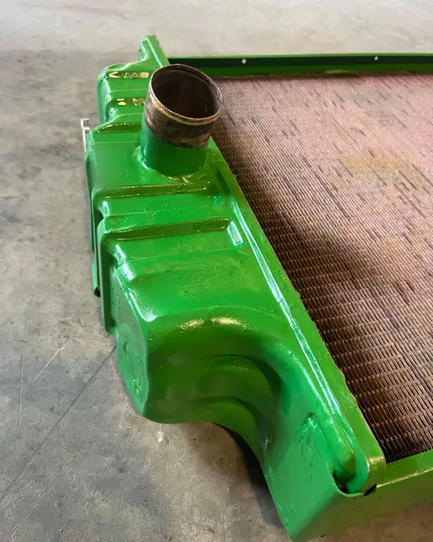 Depósito superior pintado de verde de un radiador, con la boca de entrada y el panal de cobre al lado, sobre el suelo.
