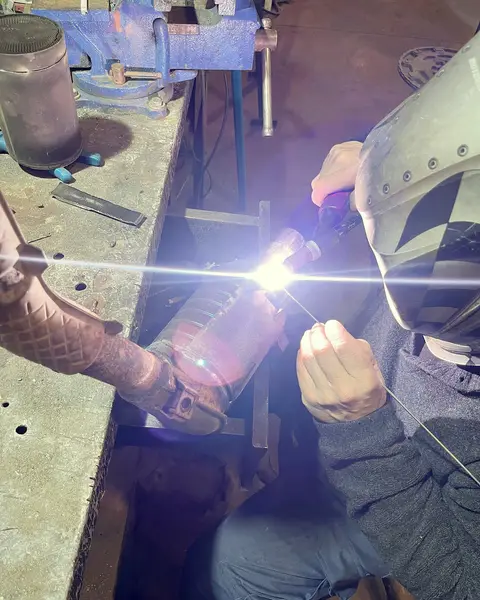 Soldador con careta haciendo una soldadura TIG sobre una pieza de escape en el taller.